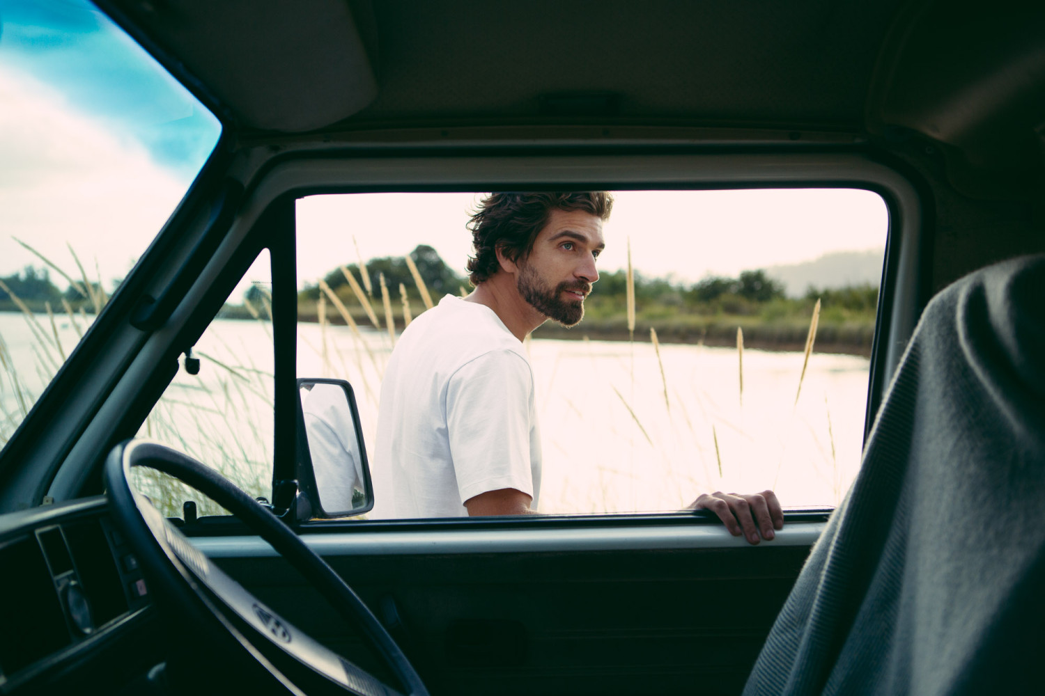 Man standing outside car near grassy field.