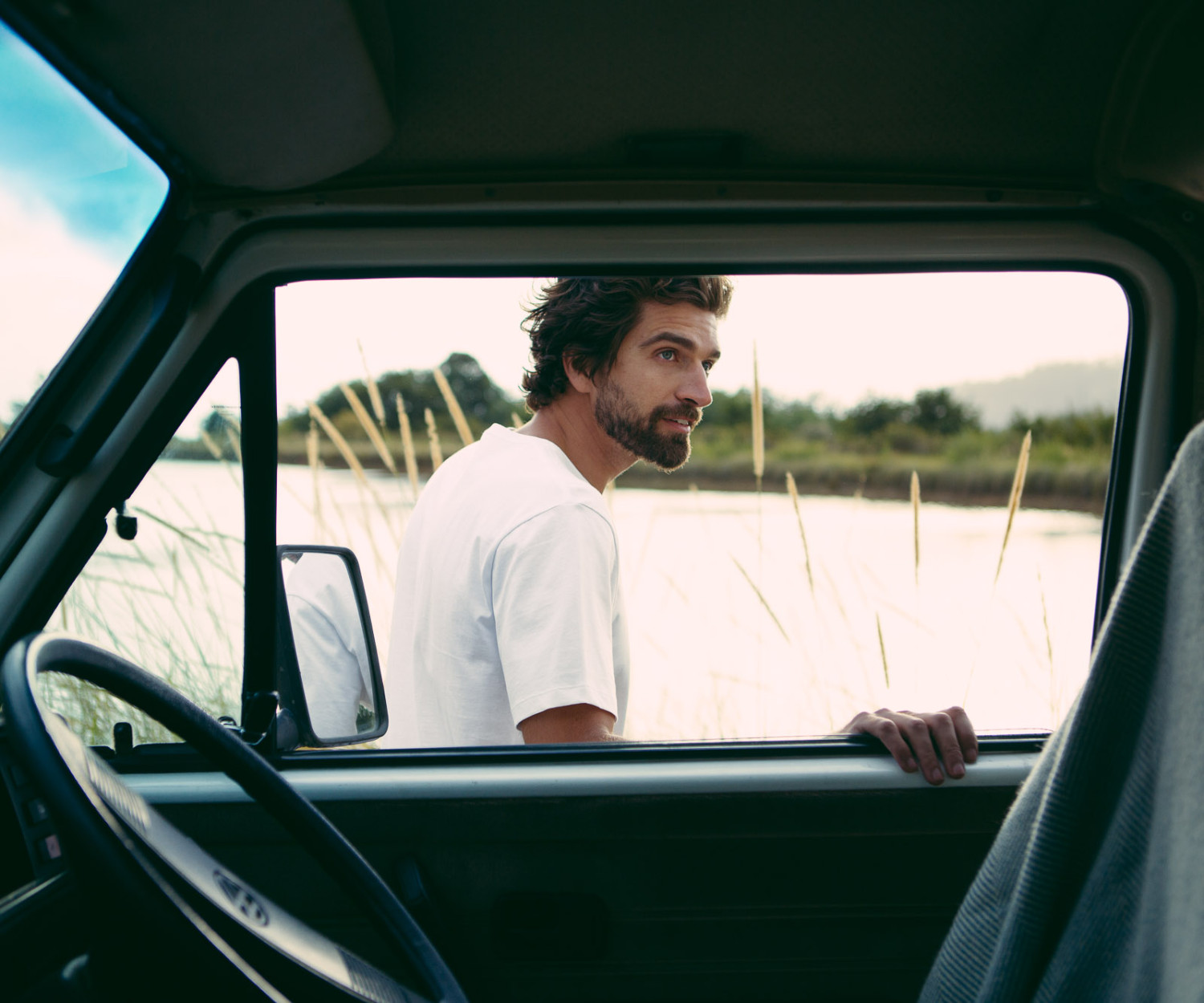 Man standing outside car near grassy field.