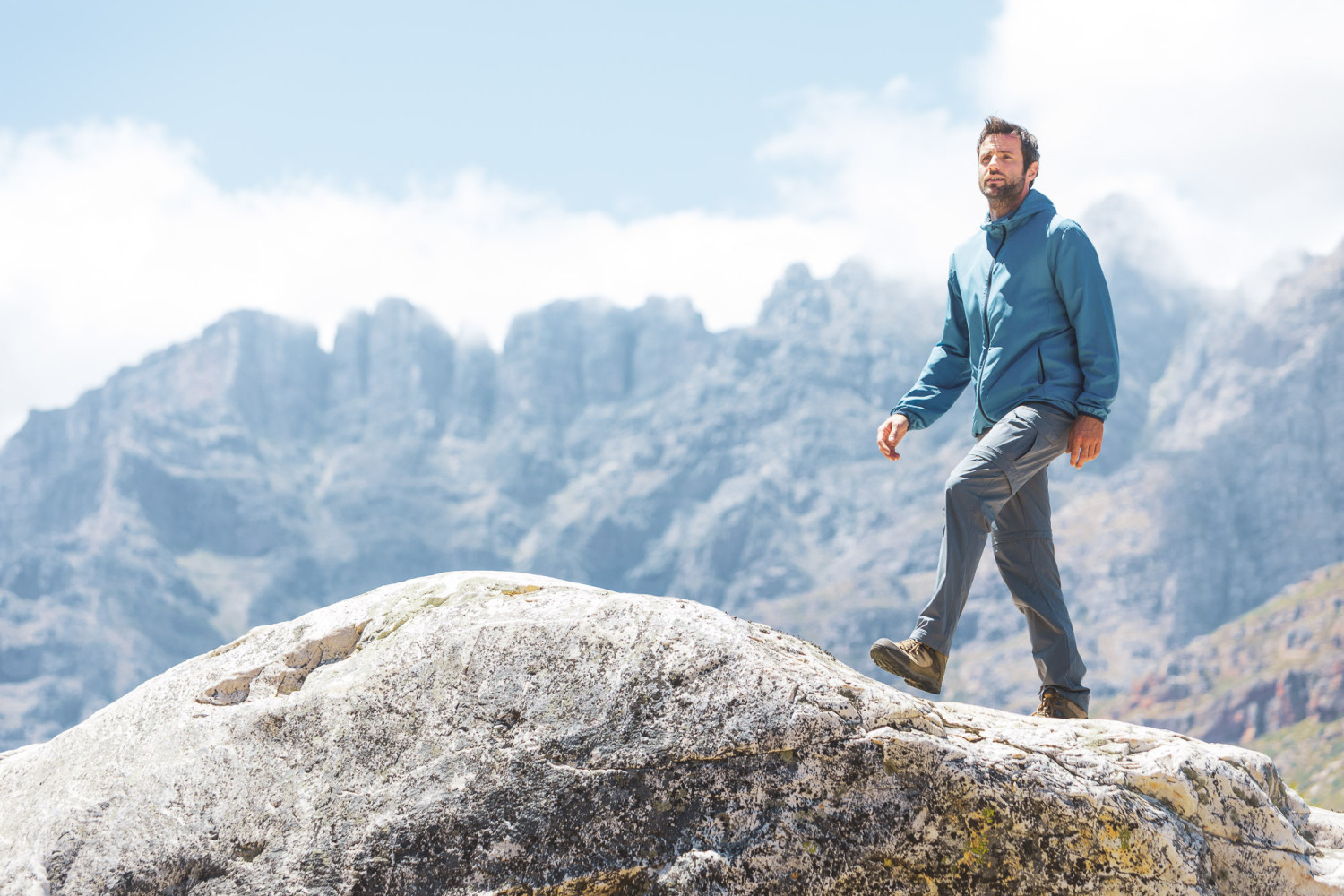 Man hiking on rock with mountains background